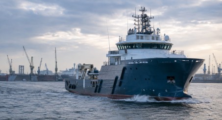 Large offshore support vessel sailing through Hamburg’s industrial harbour, with shipyard cranes in the background.